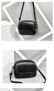 Close-up of black pebble leather crossbody bag with white stitching and triple zippers