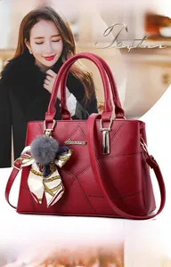 Détail d'un cabas en cuir rouge avec coutures, poignées dorées et breloque pompon en fourrure