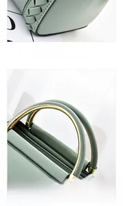 Detail of light green leather handbag featuring golden ring handle and woven stitching