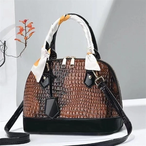 Detail einer braunen Krokodil-Muschel-Tasche mit schwarzem Lackbesatz und Seidenschal-Griff