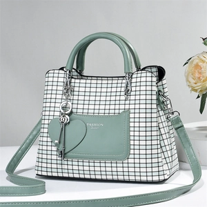 Detail view of mint green plaid handbag with heart pendant and long shoulder strap