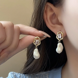 Elegant gold earrings with baroque pearl and clear crystal detail on a female model