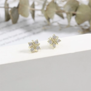 Détail de boucles d'oreilles dorées en croix avec zircons sur un support blanc