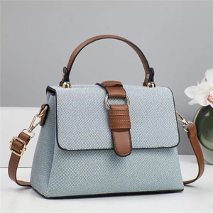 Detail of light blue textured tote bag with brown leather strap and gold ring hardware
