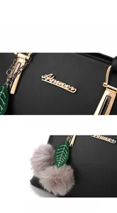 Détail du sac à main noir en cuir grainé avec logo doré et pompon en fourrure grise