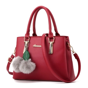 Détail du sac à main rouge en cuir avec logo doré, bandoulière et accessoire à pompon feuille