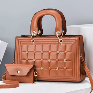 Detalle de bolso shopper acolchado marrón con tachuelas y sobre de mano a juego