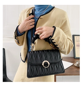 Détail du sac matelassé noir avec boucle dorée perlée et poignée plissée élégante