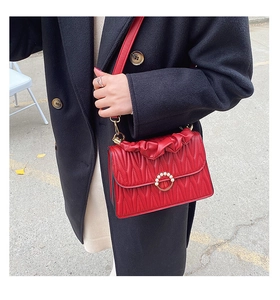 Détail du sac en cuir rouge avec boucle dorée perlée et poignée plissée élégante