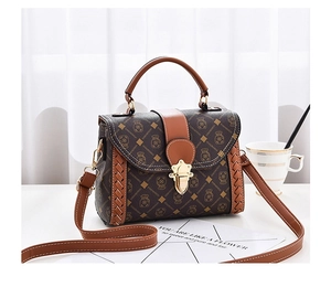 Detailed view of woven leather side trim and retro gold lock on a brown crossbody bag