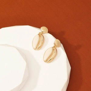 Boucles d'oreilles coquillage dorées sur support géométrique avec fond en tissu orange