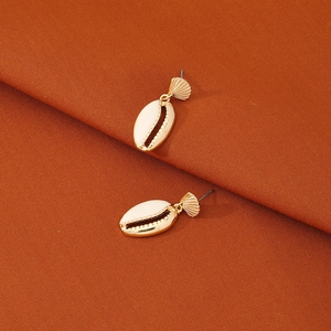 Boucles d'oreilles dorées en forme de coquillage blanc sur fond en tissu orange