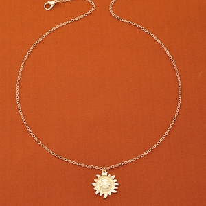 Gros plan du pendentif soleil doré avec rayons texturés sur fond de tissu orange chaud