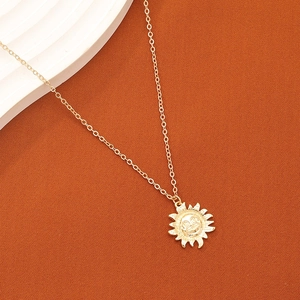 Collier doré avec pendentif visage de soleil sur fond texturé de couleur caramel