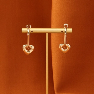 Polished gold heart drop earrings displayed on a minimalist metal stand with warm texture