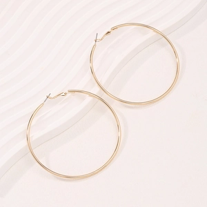 Minimalist large golden hoop earrings with a polished metallic finish on a textured background