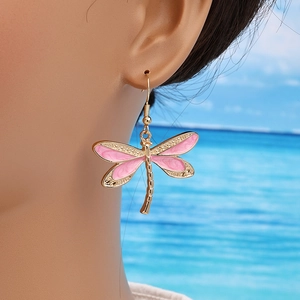 Pink enamel dragonfly earrings with gold finish, dangling style on a model shown outdoors