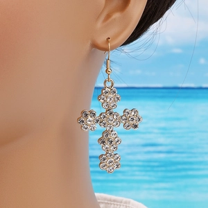 Boucles d'oreilles croix dorées élégantes avec cristaux scintillants sur un mannequin à la plage