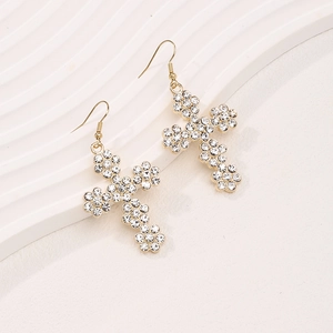 Boucles d'oreilles croix dorées élégantes avec cristaux fleurs sur fond blanc texturé