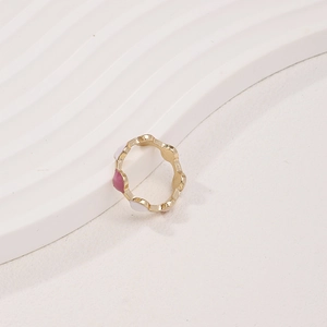 Dettaglio di un anello dorato ondulato con eleganti punti in smalto rosa e bianco