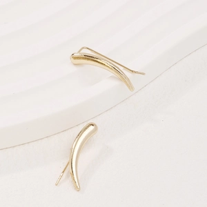 Minimalist gold curved streamline stud earrings on a textured white artistic display