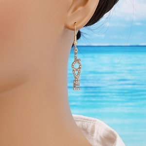 Élégantes boucles d'oreilles dorées LOVE avec strass brillants portées par un mannequin