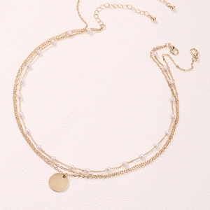 Détail d'un collier multicouche doré avec perles, médaille ronde et fermoir mousqueton