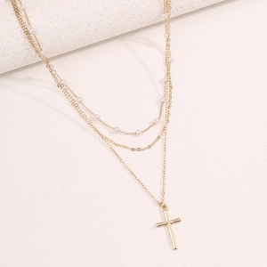 Close-up of golden multi-layer necklace with white pearls and a cross pendant detail