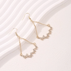 Elegant gold butterfly tassel drop earrings with white crystals on a white textured background
