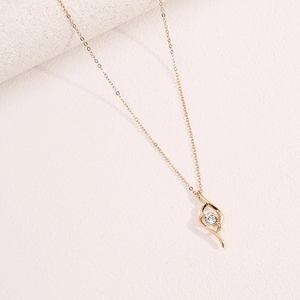 Close-up of minimalist 18K gold pendant necklace with white zircon on stone background