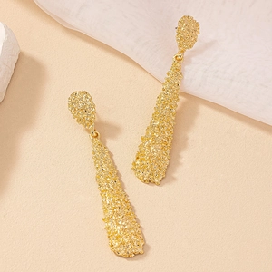 Macro shot of long irregular textured gold dangle earrings on aesthetic background
