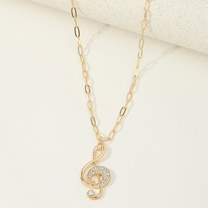 Detailed macro view of a gold musical treble clef pendant with crystals on paperclip chain