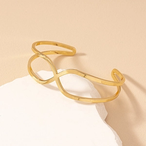 Elegant gold-tone geometric crossover open bracelet displayed on a white textured stone base
