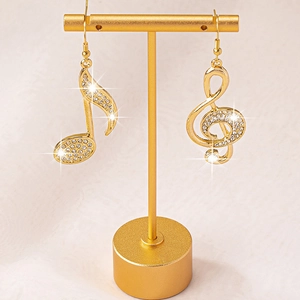 Sparkling rhinestone musical note earrings on a gold display stand with a warm tone