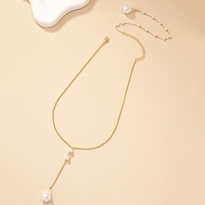Detailed shot of a gold Y-shaped necklace with baroque pearls on a beige background