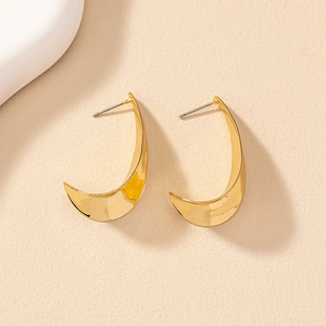 Close-up of polished gold-finished C-shape geometric hoop earrings on a textured background