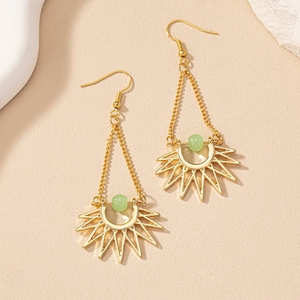 Detail view of gold bohemian sun drop earrings with a pale green bead on stone background