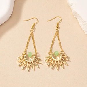 Close-up of bohemian gold sun earrings with green beads on a textured background