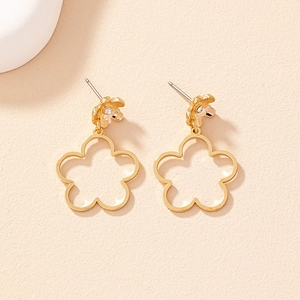 Elegant gold hollow flower drop earrings with crystal center on a cream background