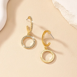 Detail shot of golden circular drop earrings with rhinestones on a beige textured background