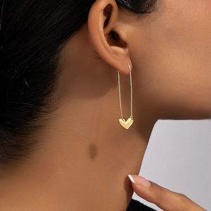 Gold safety pin earrings with polished heart pendant shown on model in a modern style