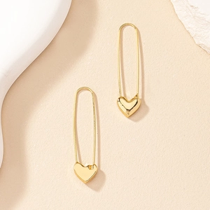 Minimalist gold heart safety pin earrings displayed on a neutral stone background