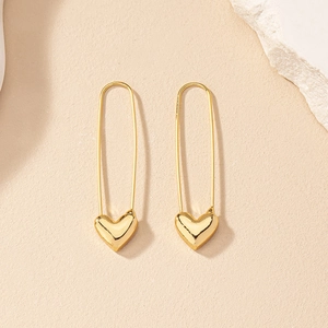 Detail of gold paperclip earrings with heart pendant on minimalist textured background