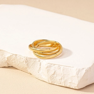 Minimalist gold trinity interlocking ring displayed on white natural stone background