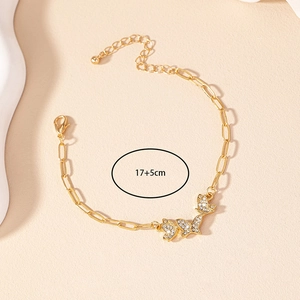 Detail of a gold butterfly bracelet with white rhinestones and a paperclip chain