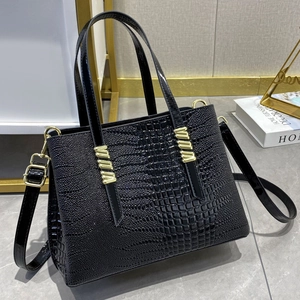 Elegante borsa tote nera goffrata coccodrillo con dettagli dorati e tracolla su marmo