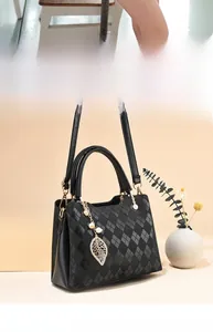 Detail of diamond-quilted tote with gold hardware and leaf pendant on warm background