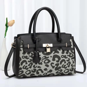 Chic women's cow print and black leather handbag with gold buckle in minimalist setting