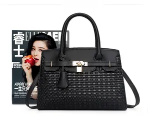 Détail d'un sac à main en cuir noir avec texture tressée, fermoir doré et un magazine