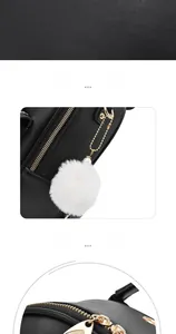Detail of black leather backpack featuring a white pompom charm and gold metal zippers